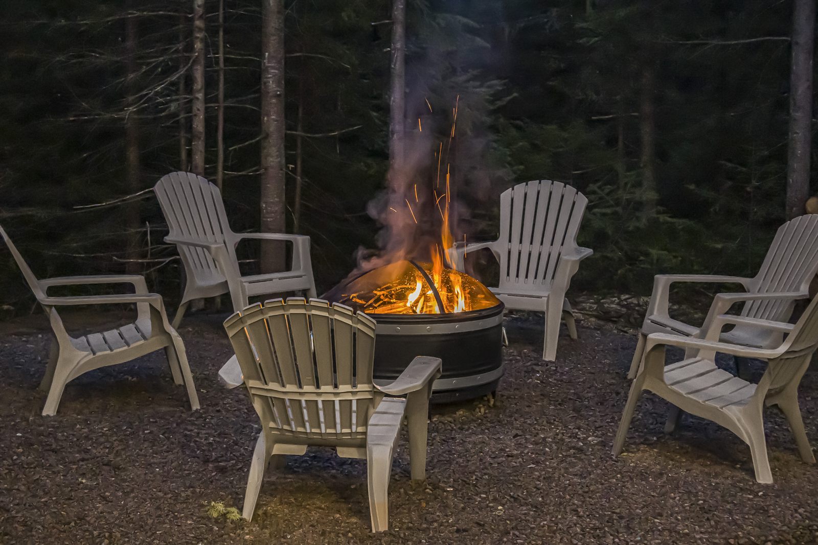 Chaises Adirondack autour d'un feu de camp en soirée, en forêt