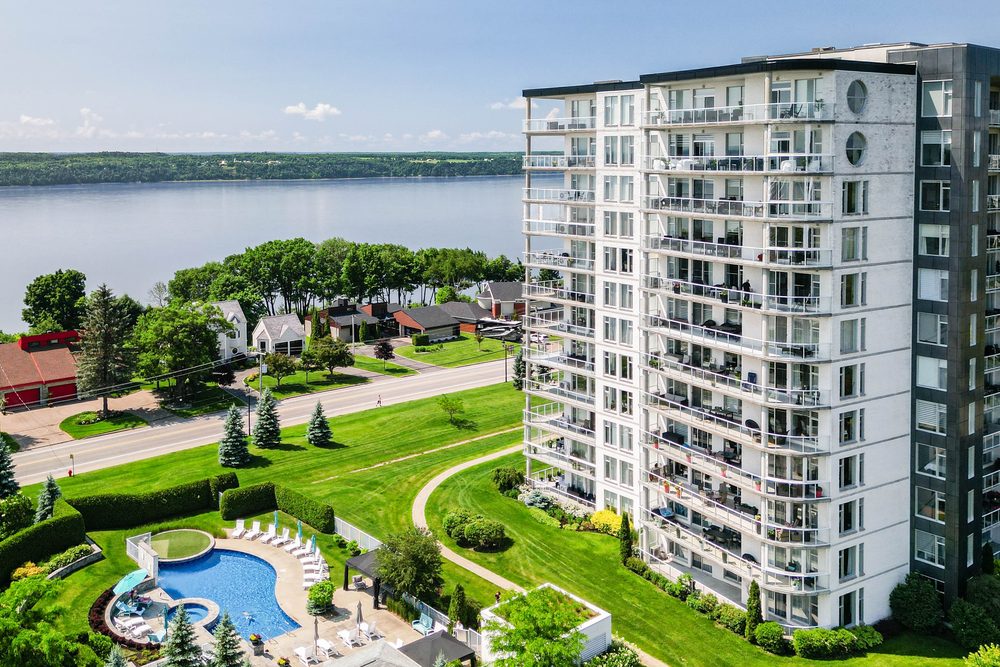 Aerial view of a riverfront condo building with outdoor pool