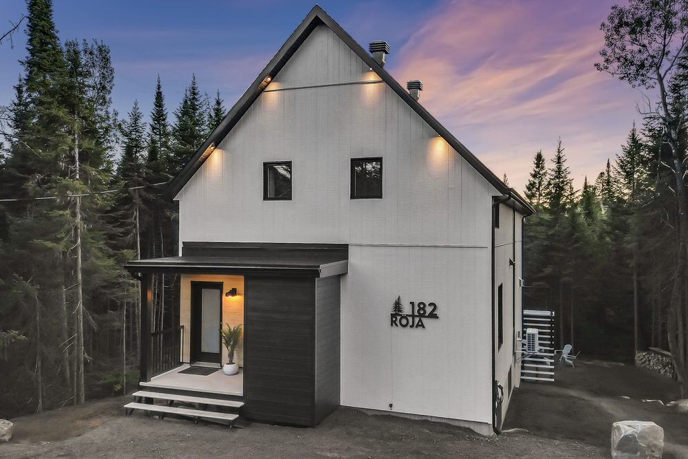 Front of a contemporary chalet in the forest, lit at dusk