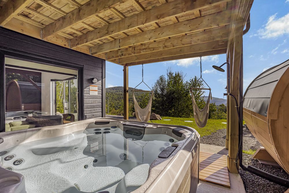 Outdoor hot tub under a pergola with sauna, hanging chairs and mountain view